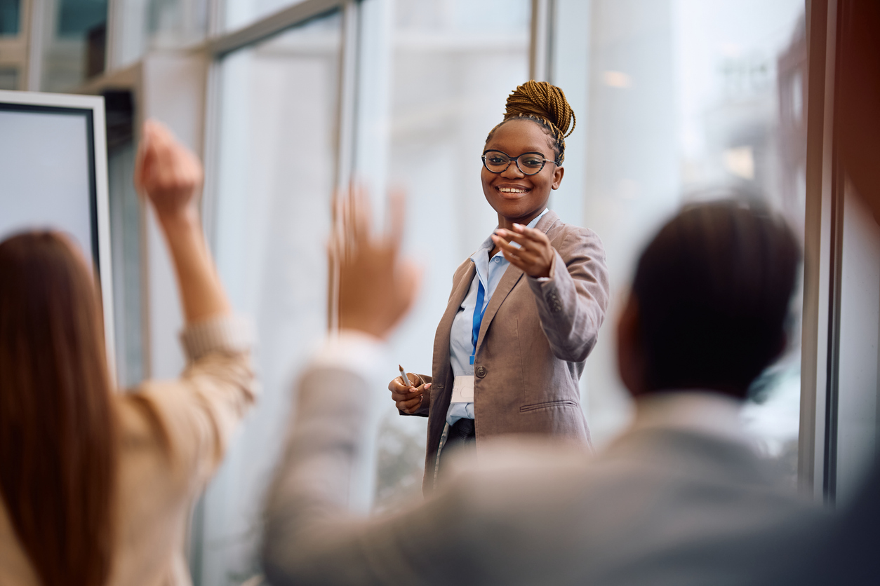 Smiling businesswoman pointing at one a colleague who wants to ask a question during a conference in board room.