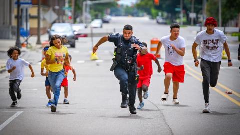 A uniformed law enforcement officer running alongside children.