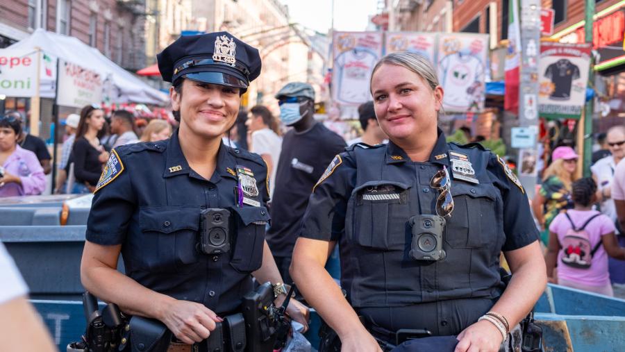 Two law enforcement officers smiling, standing in front of a community event.