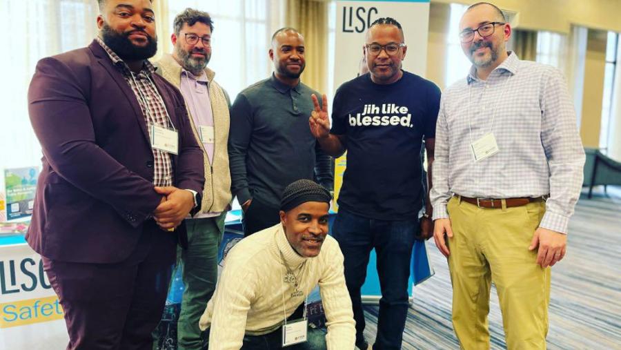 A group of men pose in front of a booth at a conference.
