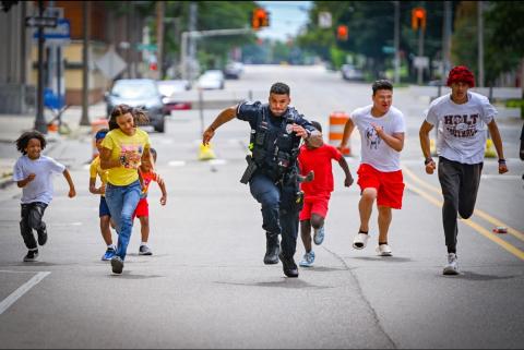 A uniformed law enforcement officer running alongside children.